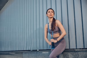 Front view of a serene fit young Caucasian female in active wear leaning against the wall