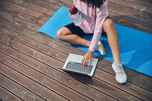 Top view of female working online on laptop while holding bottle of water in her hand