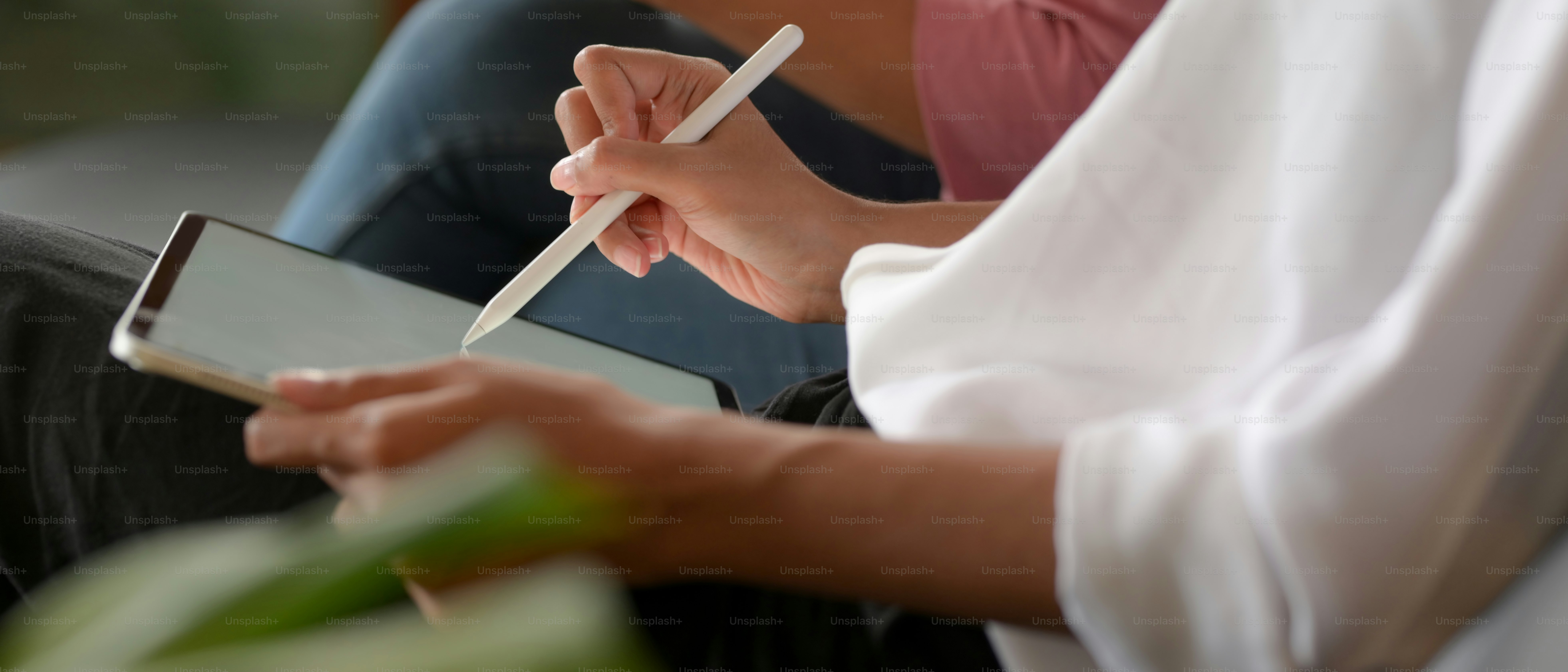 Side view of female worker writing on mock up tablet while meeting with her colleague
