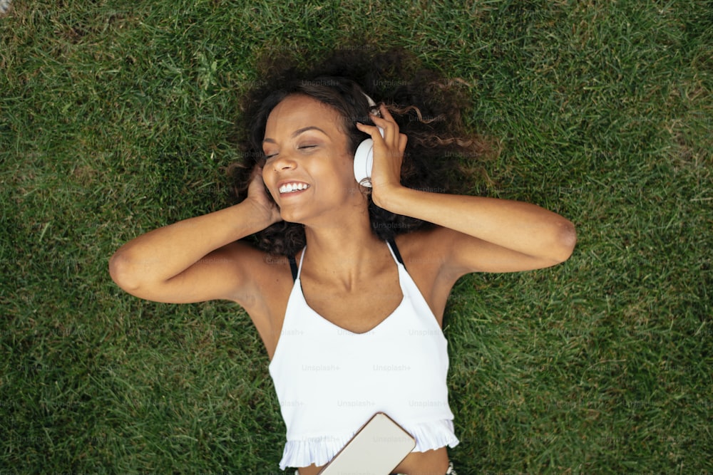 Menina africana nova deitada na grama e ouvindo música