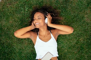 Young african girl lying on grass and listening music