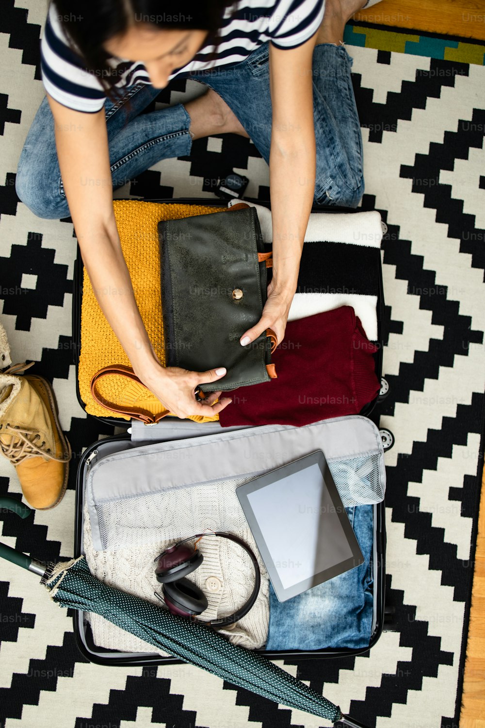 Young woman tourist packing her winter and autumn warm stuff into a big suitcase. Traveling preparation concept. View from above or top view.