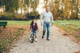 Happy father and his daughter walking in the park with a bike and smile at camera