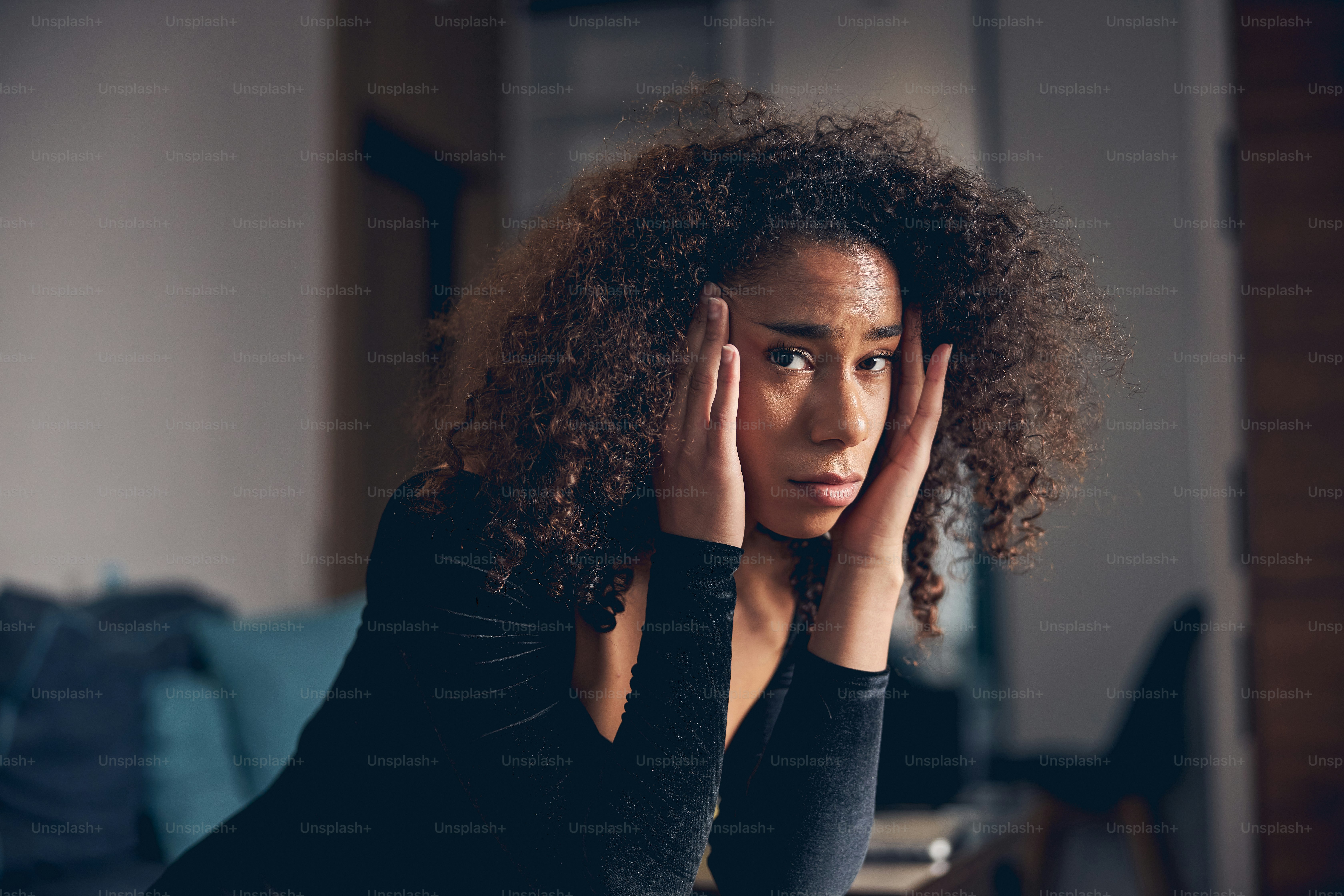 Portrait of a depressed young lady with curly dark hair touching her temples with fingers