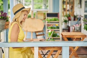 Side view of a smiling mature female freelancer working on her laptop on the veranda