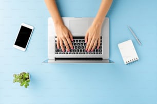 青いオフィスのデスクトップでラップトップを使用する女性の手の俯瞰ショット。ビジネスの背景。フラットレイ