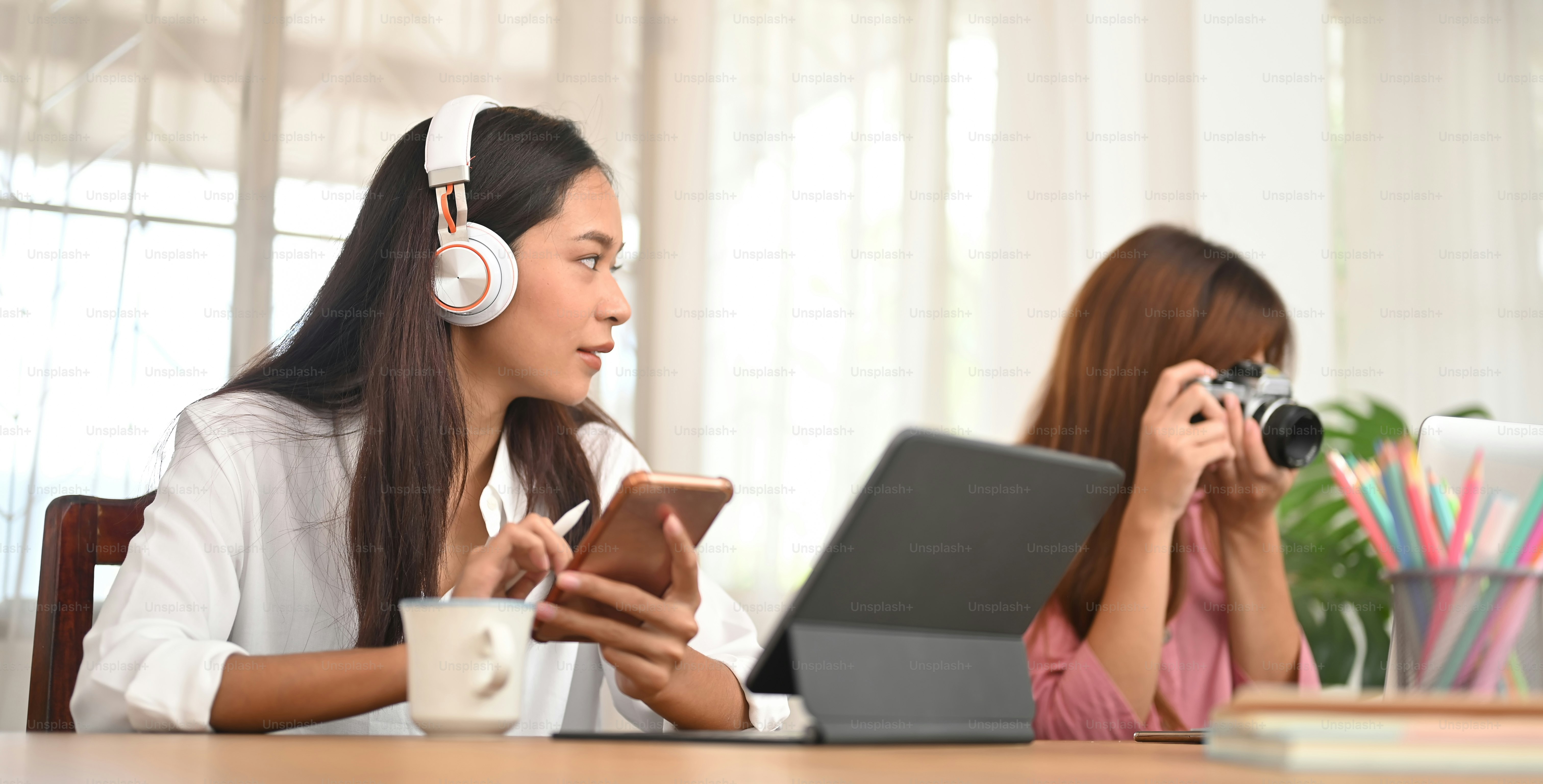 Fotografinnen arbeiten mit einem Computer-Tablet und einem Laptop am hölzernen Schreibtisch zusammen.