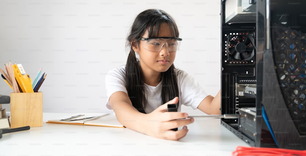 어린 소녀가 흰색 작업 테이블에서 컴퓨터 하드웨어를 수리하고 있습니다.