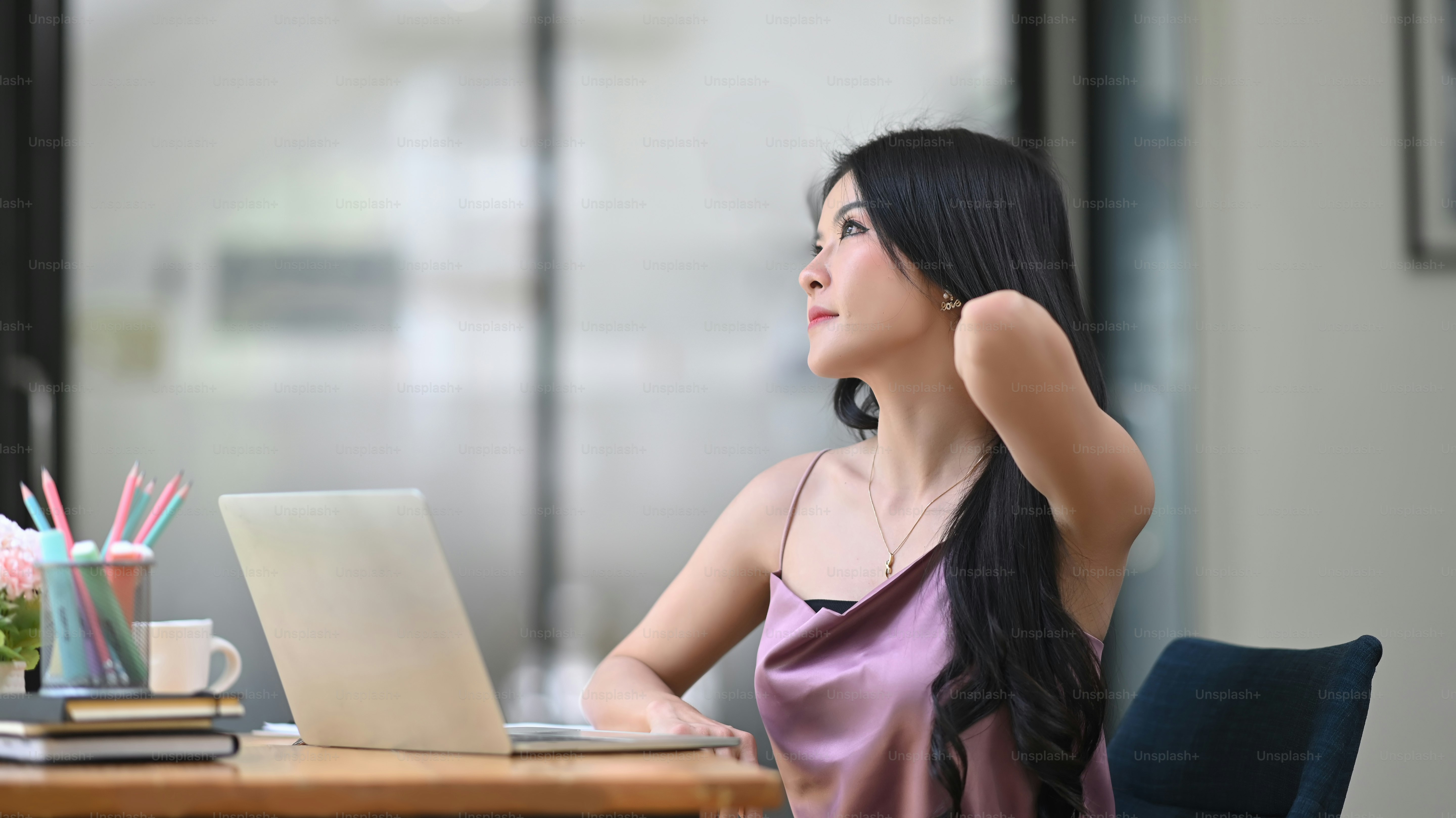 A beautiful woman is stretching her arm while relaxing at the working table.