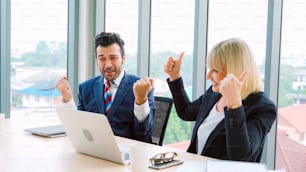 Two happy business people celebrate at office meeting room. Successful businessman congratulate project success with colleague at modern workplace while having conversation on financial data report.