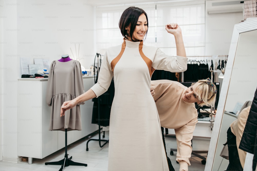 ファッションスタジオで女性モデルと新しいトレンディなドレスで顧客と作業するプロのデザイナー。クリエイティブな人々のコンセプト。