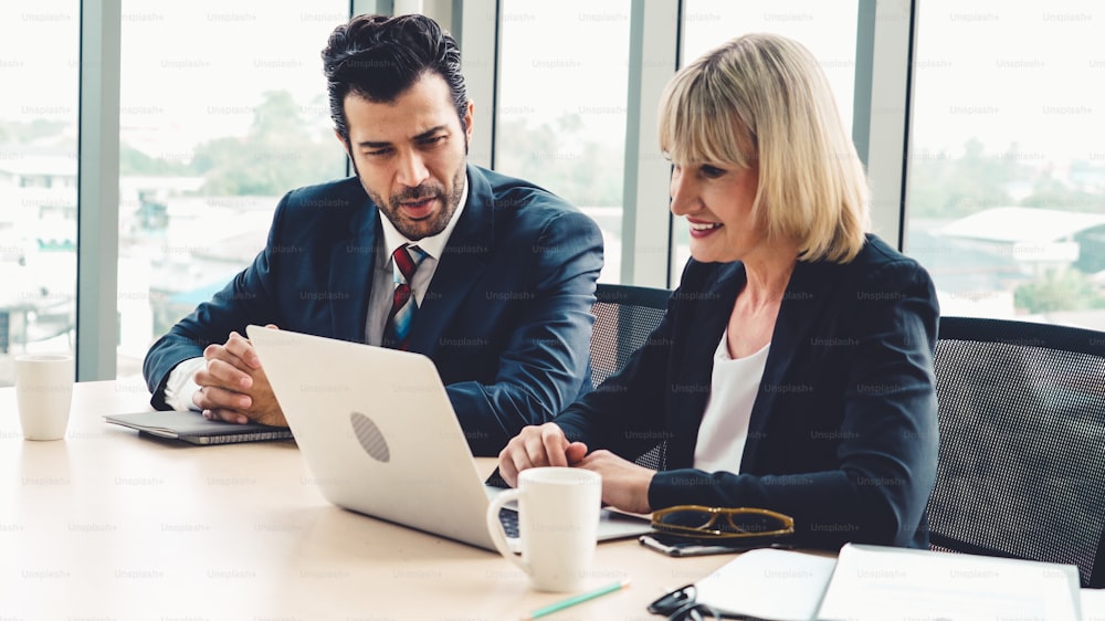 Two business people talk project strategy at office meeting room. Businessman discuss project planning with colleague at modern workplace while having conversation and advice on financial data report.