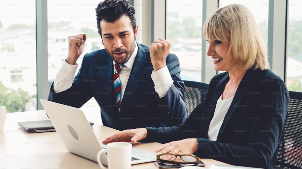 Two happy business people celebrate at office meeting room. Successful businessman congratulate project success with colleague at modern workplace while having conversation on financial data report.