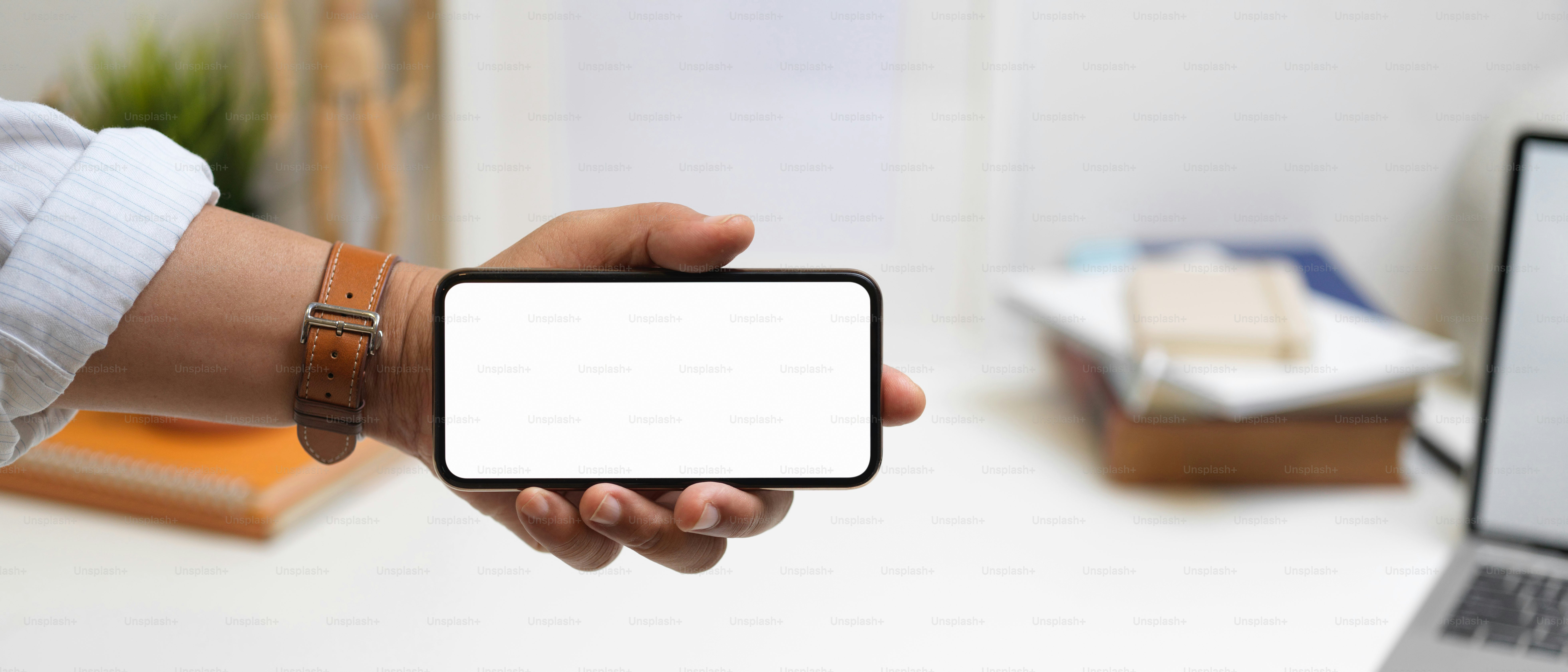 Nahaufnahme der männlichen Hand, die ein horizontales Smartphone mit Clipping-Pfad im Büroraum hält