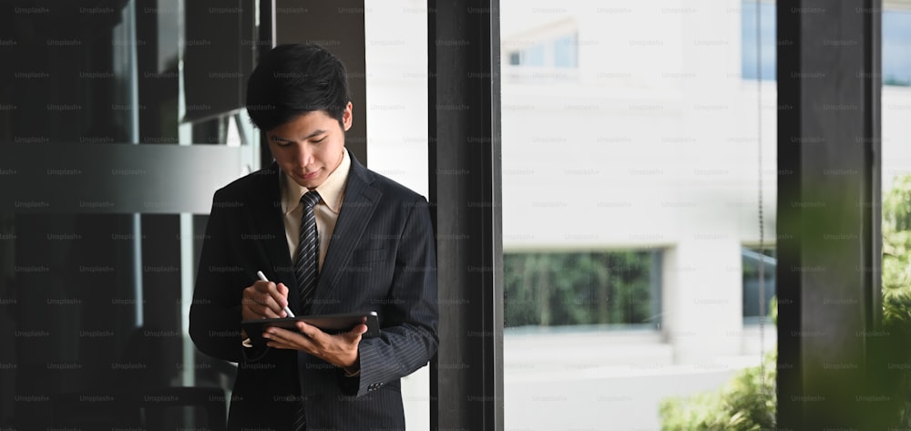 Un uomo d'affari sta usando un tablet per computer e si trova sopra l'ufficio moderno come sfondo.