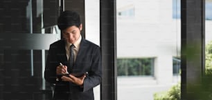 A businessman is using a computer tablet and standing over the modern office as a background.