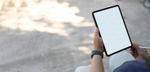 A cropped image of hands is using a white blank screen computer tablet and stylus pen outside the home.