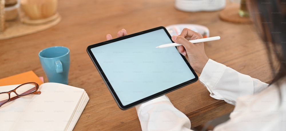 Das abgeschnittene Bild der Hände einer Frau verwendet ein weißes Computer-Tablet auf dem Holztisch.