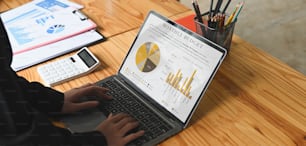 Cropped image of Businesspeople is using a computer laptop with graphic charts on screen at the wooden desk.