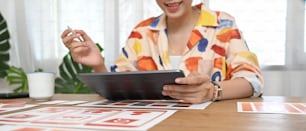 A graphic developer is using a computer tablet and stylus pen at the wooden working desk.