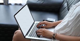 Cropped image of a woman is using a white blank screen laptop while sitting on the sofa.