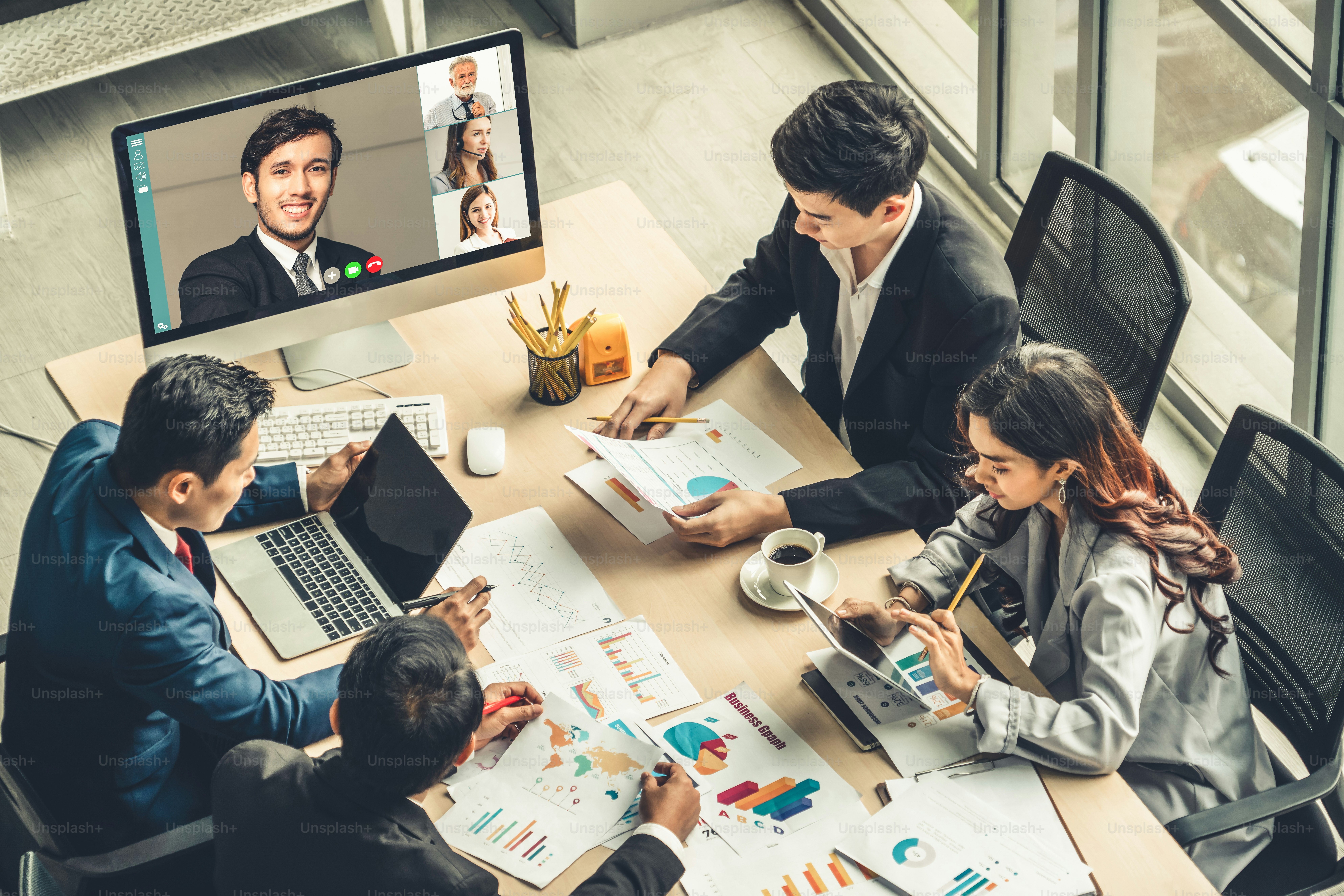A team of four people in a meeting with a video conference on screen