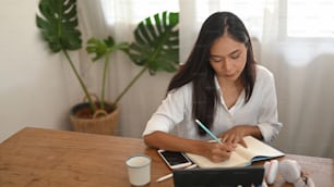 Uma bela mulher está tomando notas enquanto está sentada à mesa de madeira.