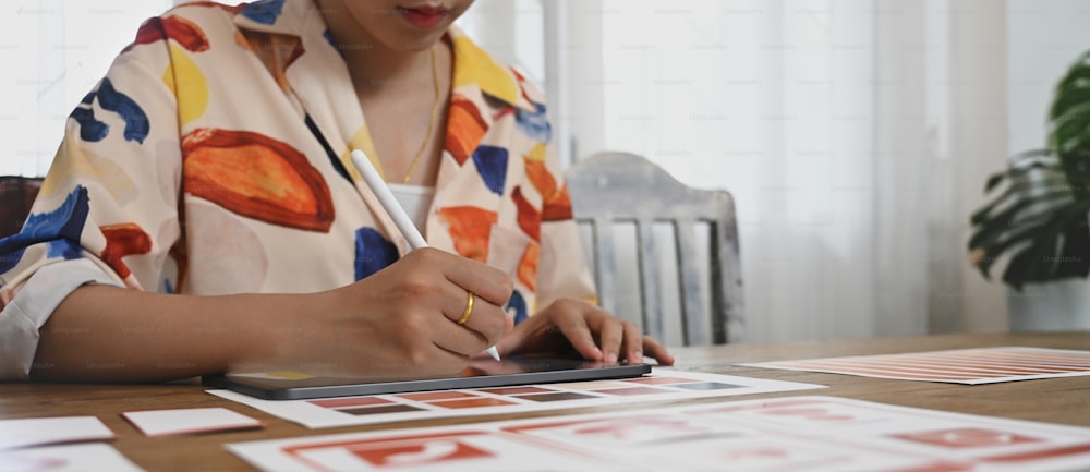 A graphic developer is using a computer tablet and stylus pen at the wooden working desk.