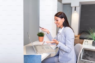 Focused business woman using laptop at home, looking at screen, chatting, reading or writing email, sitting on couch, smiling female student doing homework, working on research project online