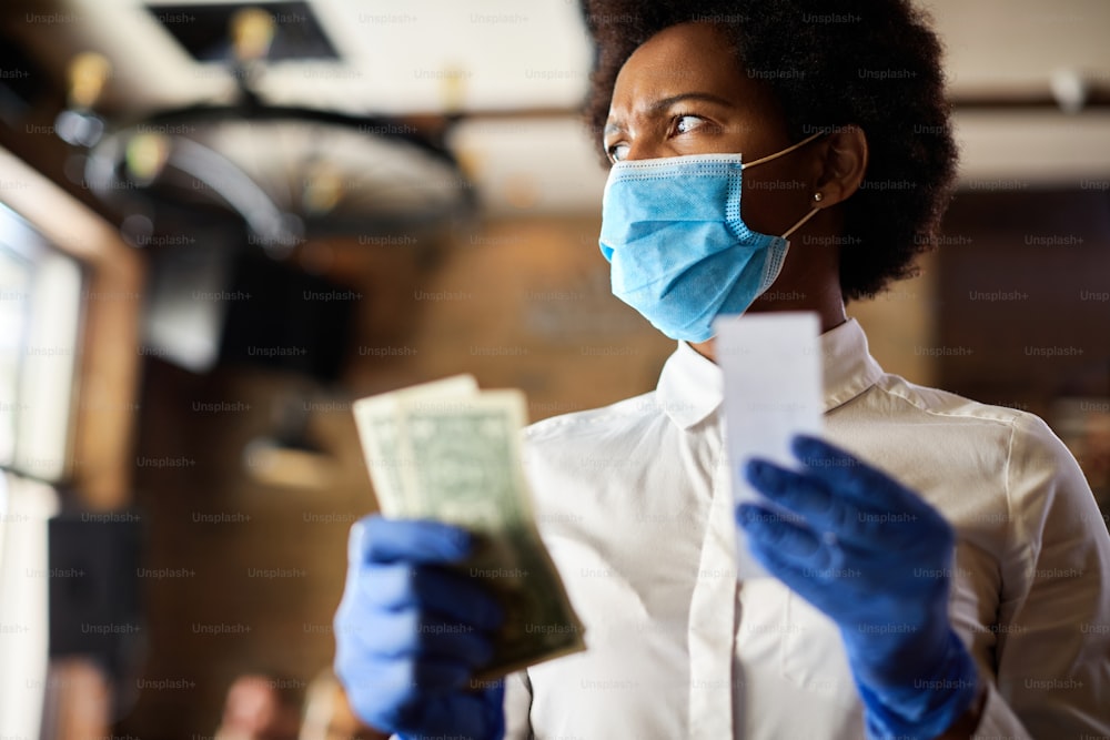 African American waitress with protective face mask and gloves feeling disappointed with a tip form her customers.