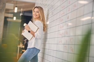 Beautiful female worker looking at camera and smiling while holding spiral sketchbook