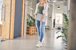 Stylish lady in jeans and sneakers holding modern silver notebook