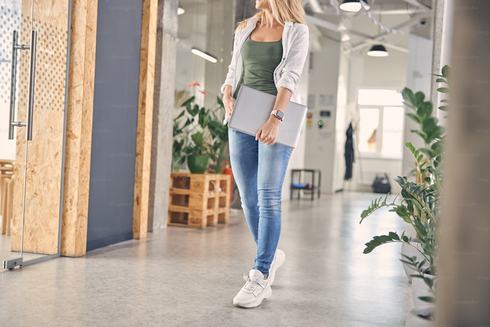 Stylish lady in jeans and sneakers holding modern silver notebook