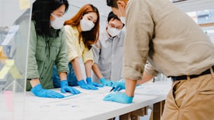 Asia businesspeople discussing business brainstorm meeting together share data, wearing face mask and glove back at work in new normal office. Lifestyle and social distancing at after coronavirus.