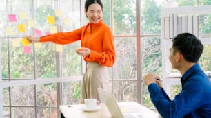 Business people work on project planning board in office and having conversation with coworker friend to analyze project development . They use sticky notes posted on glass wall to make it organized .