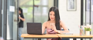 A beautiful woman is holding a glass of water while sitting at the wooden table.