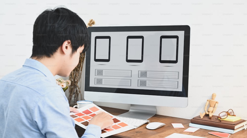 Un grafico sta selezionando un colore mentre è seduto davanti a un computer al tavolo di legno.