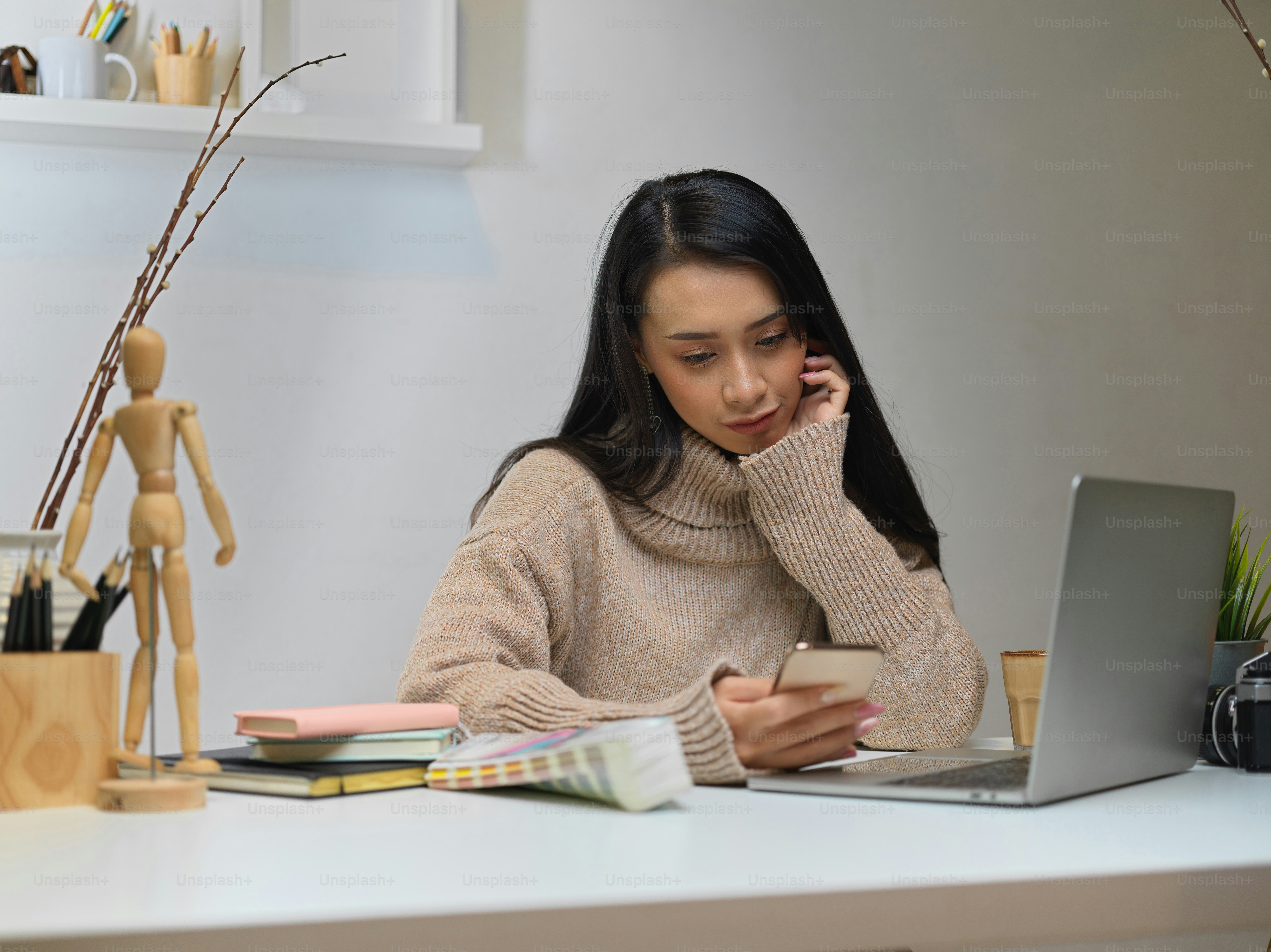 Portrait of female office worker sitting at office desk while using smartphone in office room