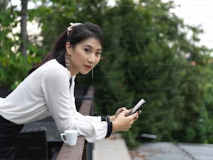 Portrait of businesswoman using smartphone while relaxed standing at balcony with garden view