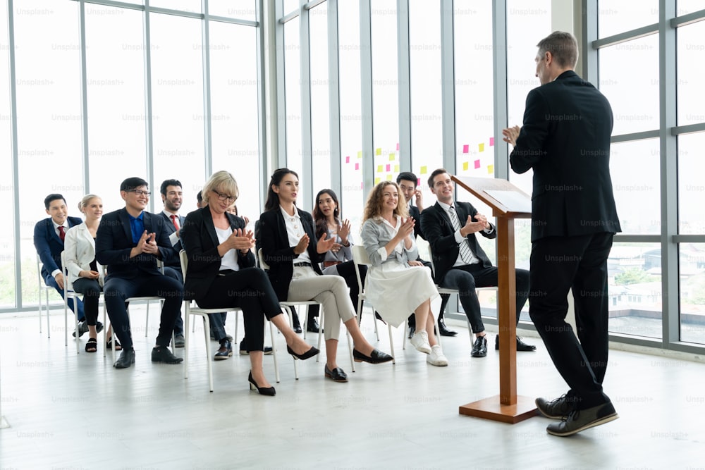 Group of business people meeting in a seminar conference . Audience listening to instructor in employee education training session . Office worker community summit forum with expert speaker .