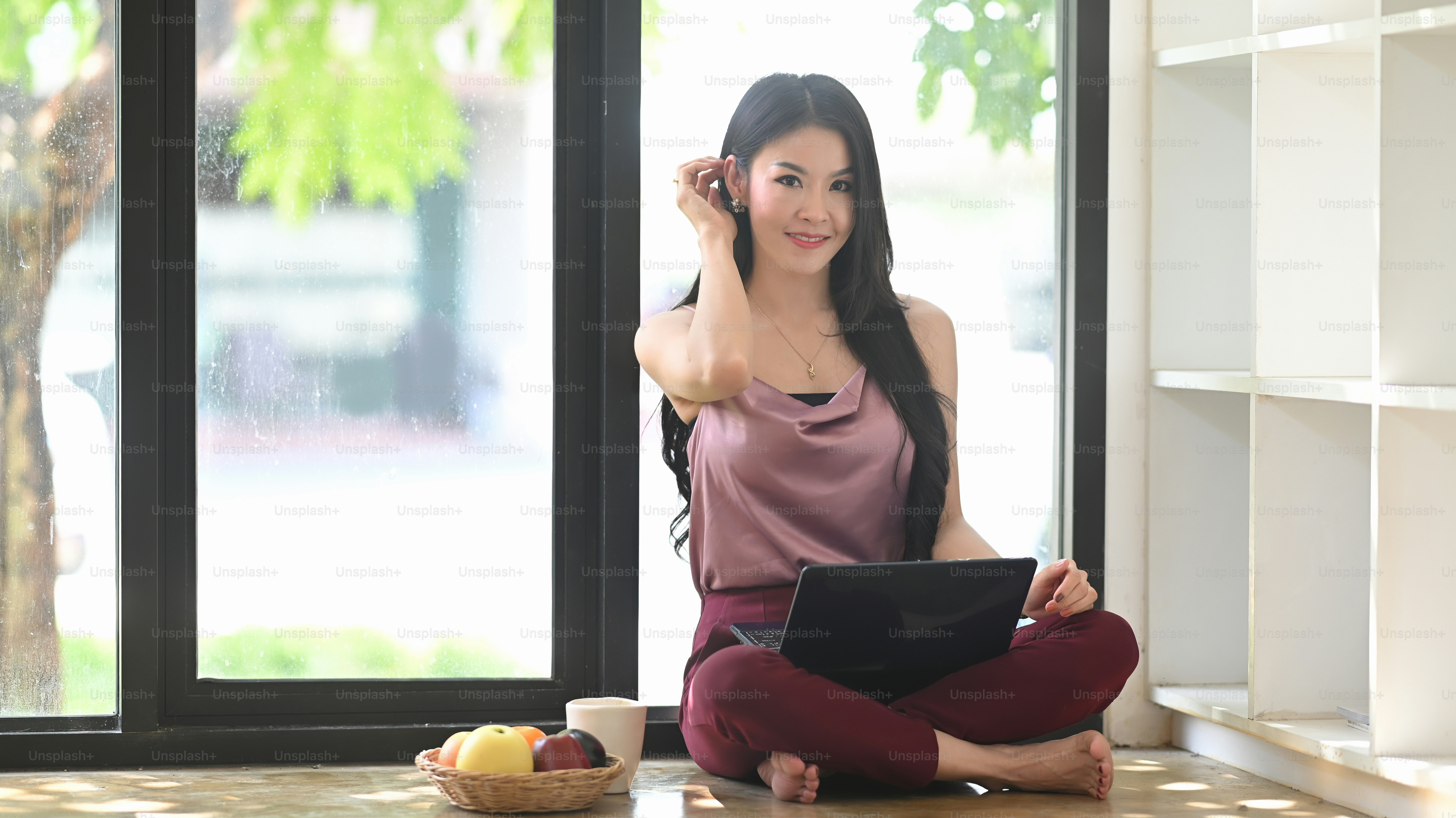 A beautiful woman is sitting on living room floor and relaxing with a computer laptop.