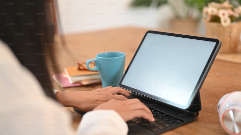 Das abgeschnittene Bild der Hände einer Frau verwendet ein weißes Computer-Tablet auf dem Holztisch.