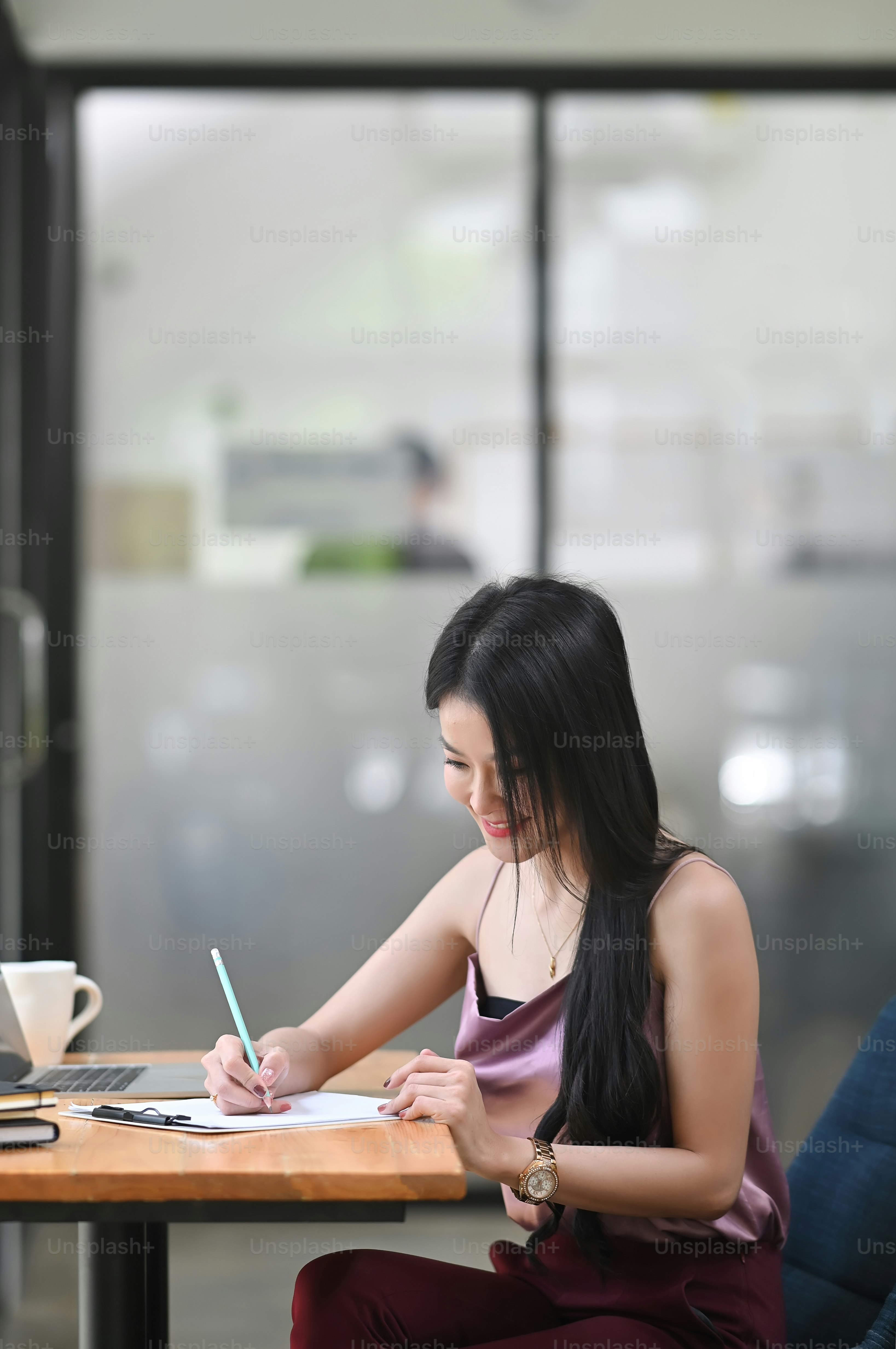 Una hermosa mujer está tomando notas en la mesa de trabajo de madera.
