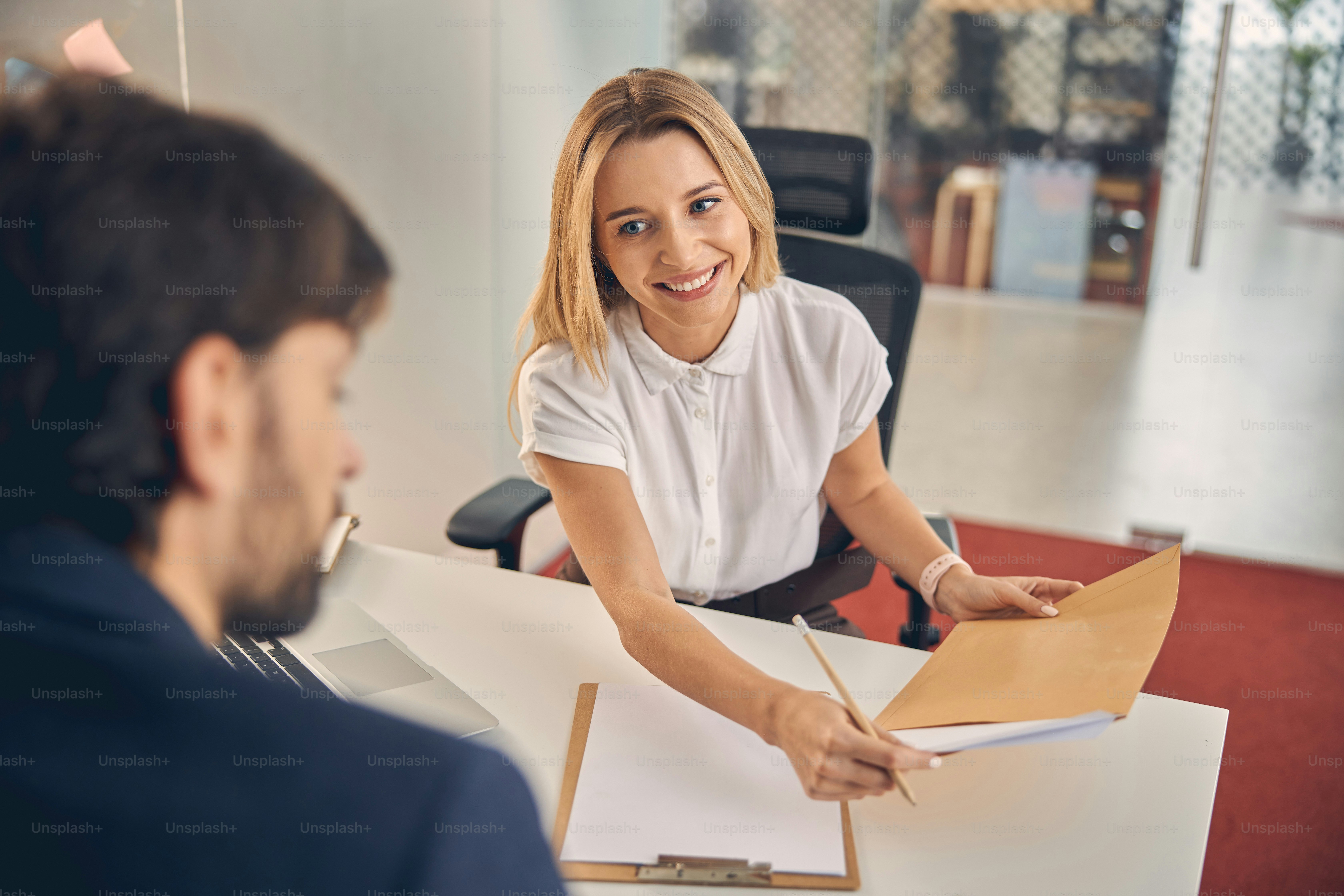 Lächelnde blonde Dame, die Bleistift und Dokumente hält, während sie dem Mann gegenüber sitzt