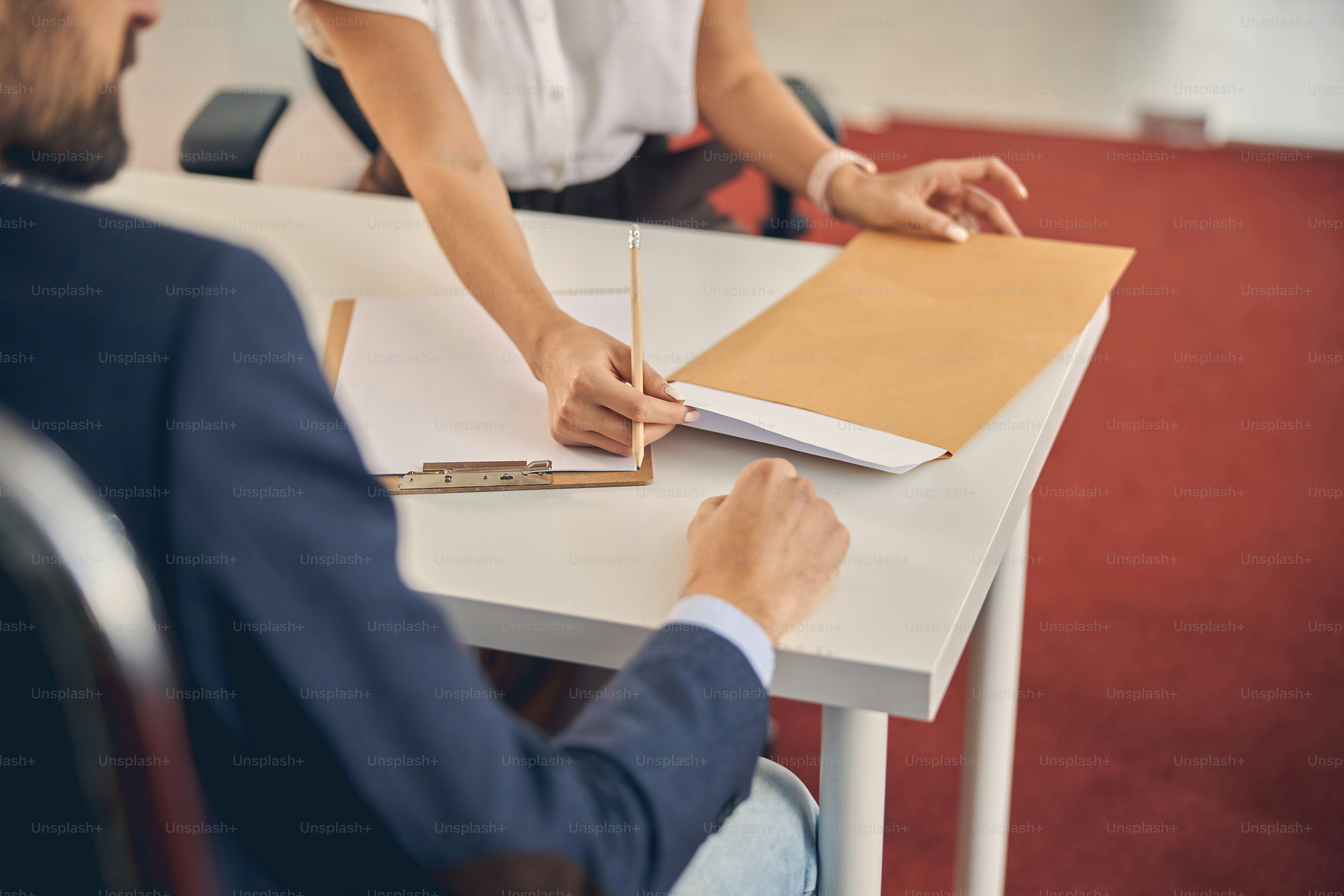 Nahaufnahme einer Arbeiterin, die ein Blatt Papier aus dem Umschlag zieht, während sie dem Mann gegenüber sitzt