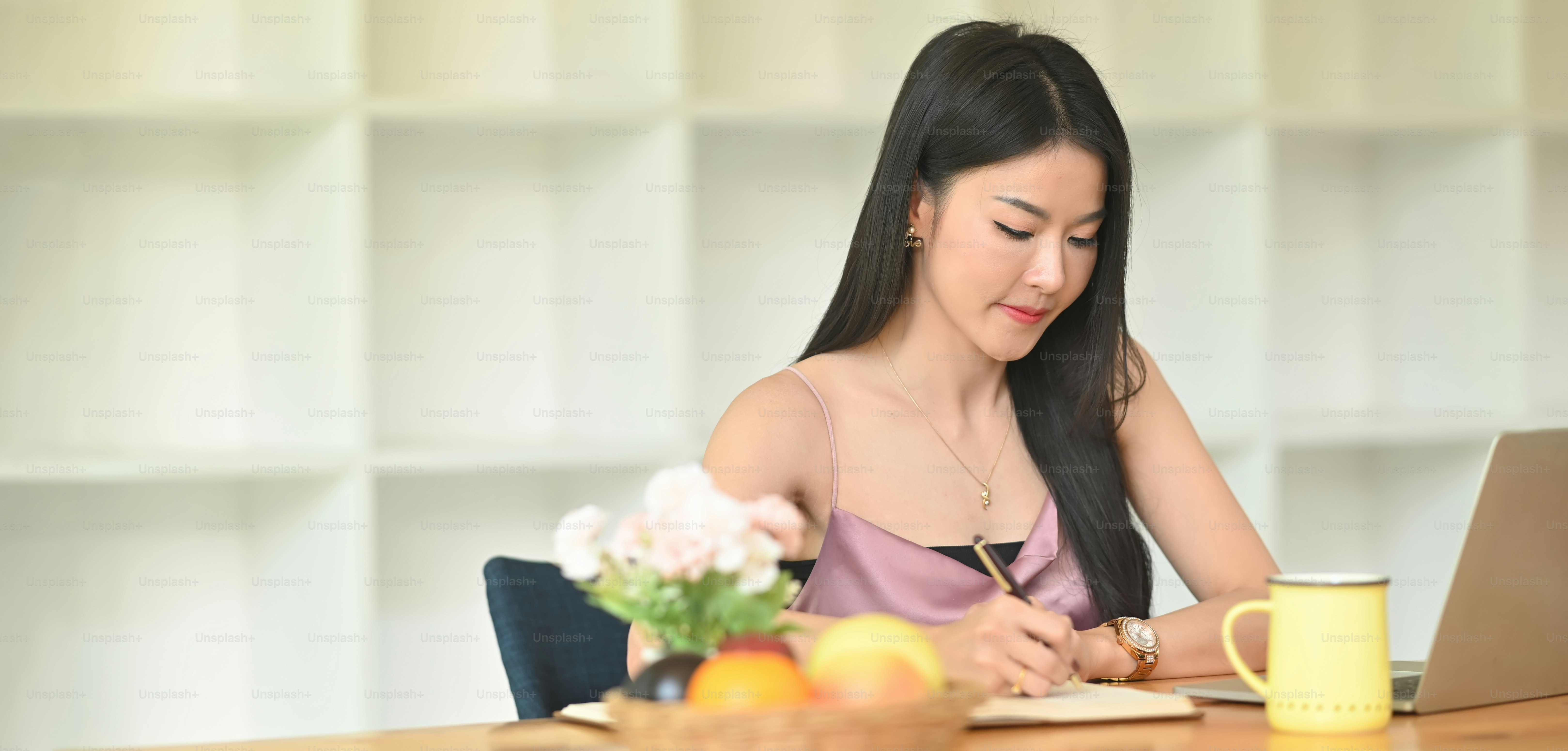 A beautiful woman is taking notes at the wooden working table.