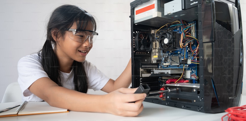 Uma garotinha está consertando hardware de computador na mesa de trabalho branca.