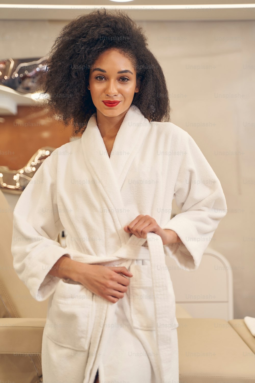 Positive attractive lady fastening her bathrobe belt while looking directly with peaceful glance