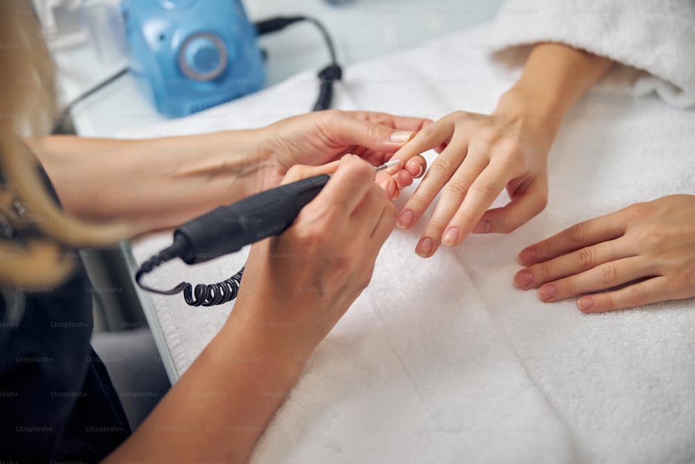 Top view close up of female hands while nail artist is removing cuticle with filing machine