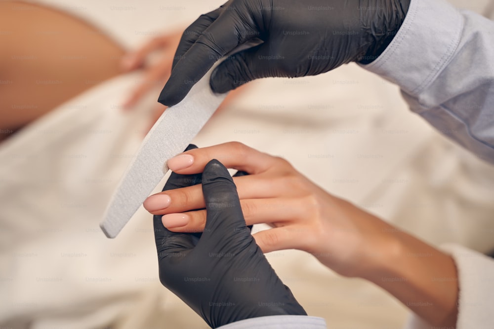 Experienced manicurist carefully shaping client nail form while using professional file